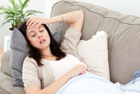 Indisposed woman feeling her temperature while resting on the sofa